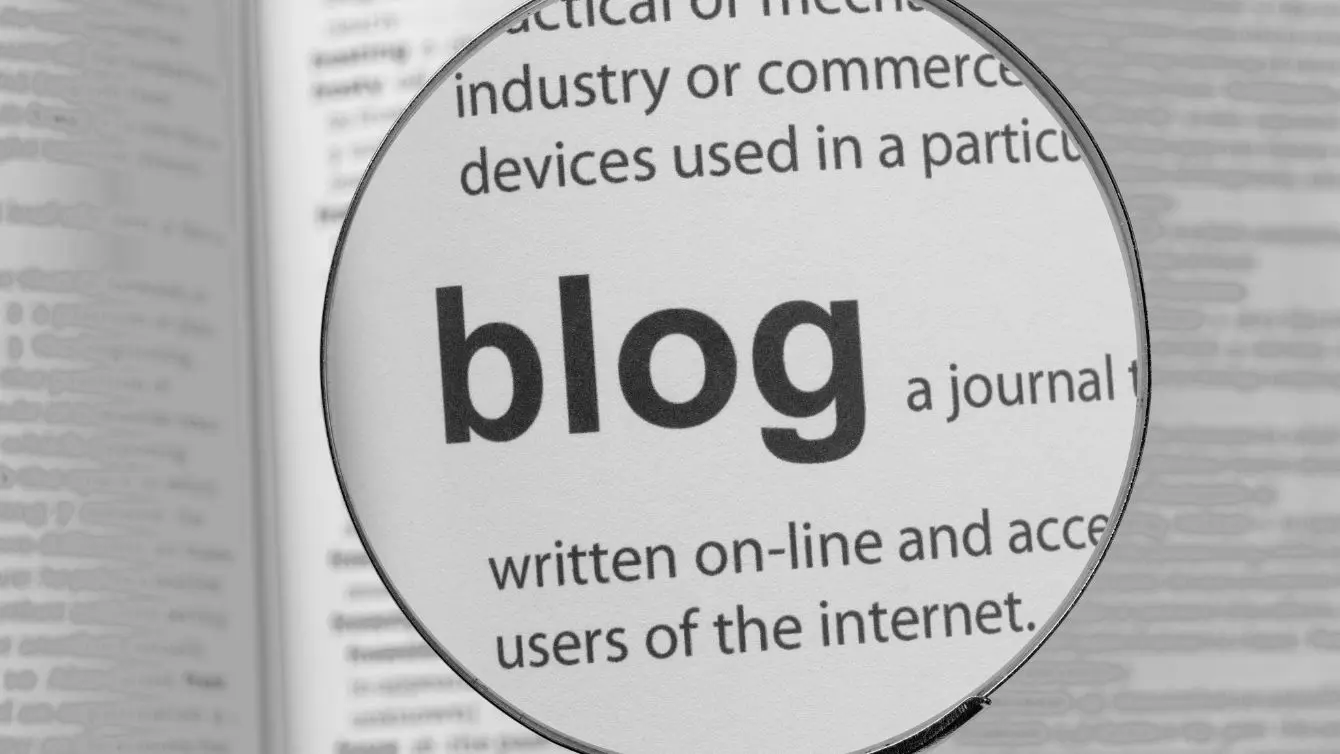 Magnifying glass focusing on the word blog in a printed dictionary, used as a background for the blog section.
