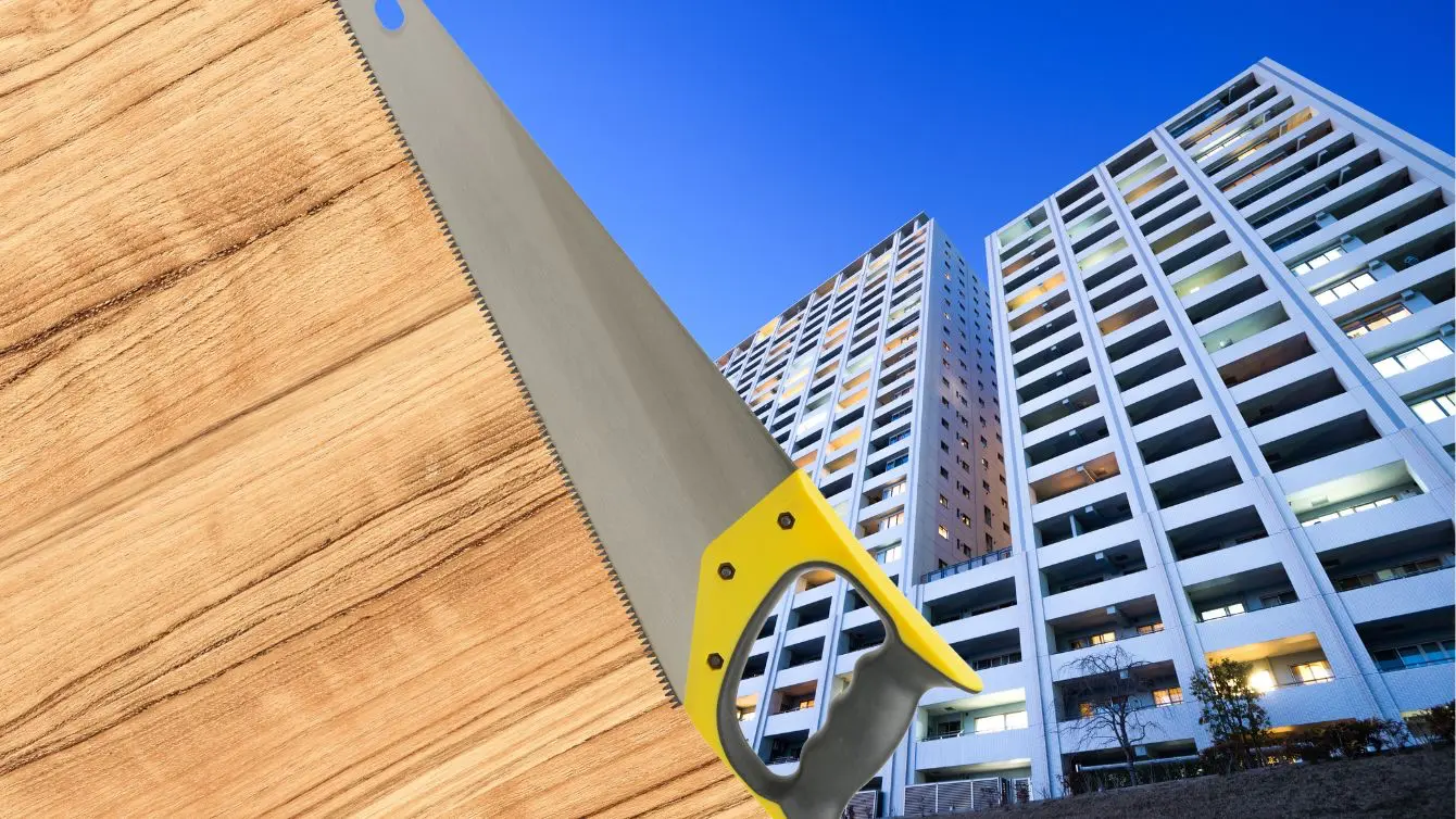 Hand saw over a wooden board with tall apartment buildings in the background, hinting at woodworking in an apartment.
