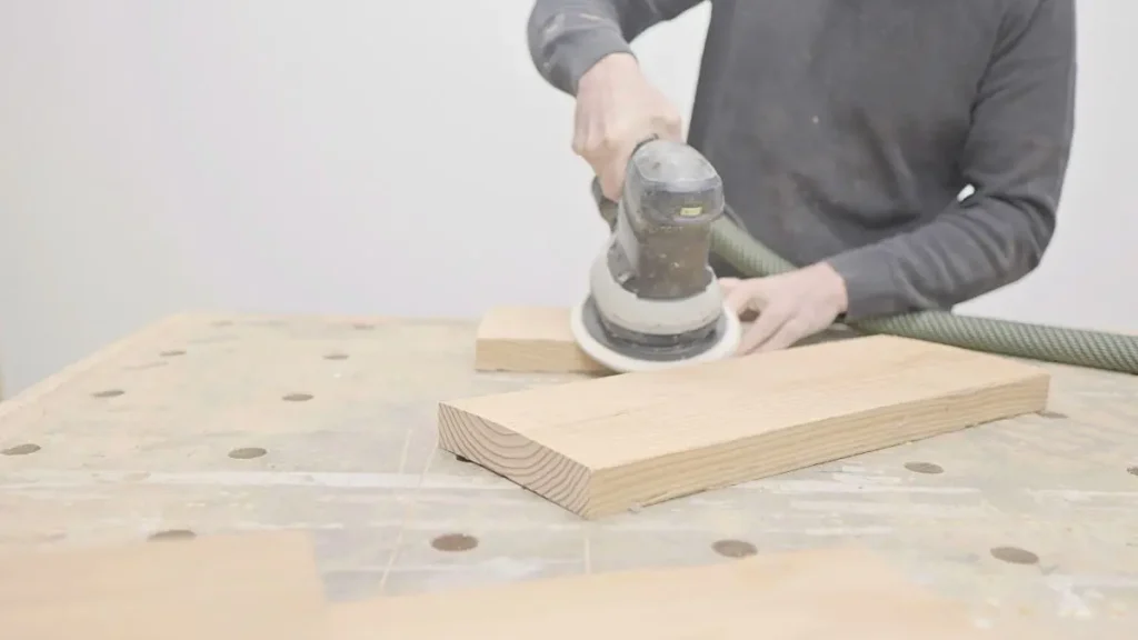 Hands sanding a wooden board with an orbital sander, woodworking for beginners project.