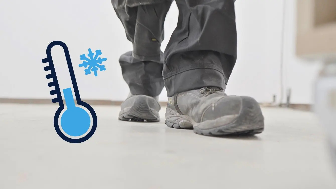 Work boots on a cold workshop floor with a blue thermometer showing how chilly concrete can feel in winter.