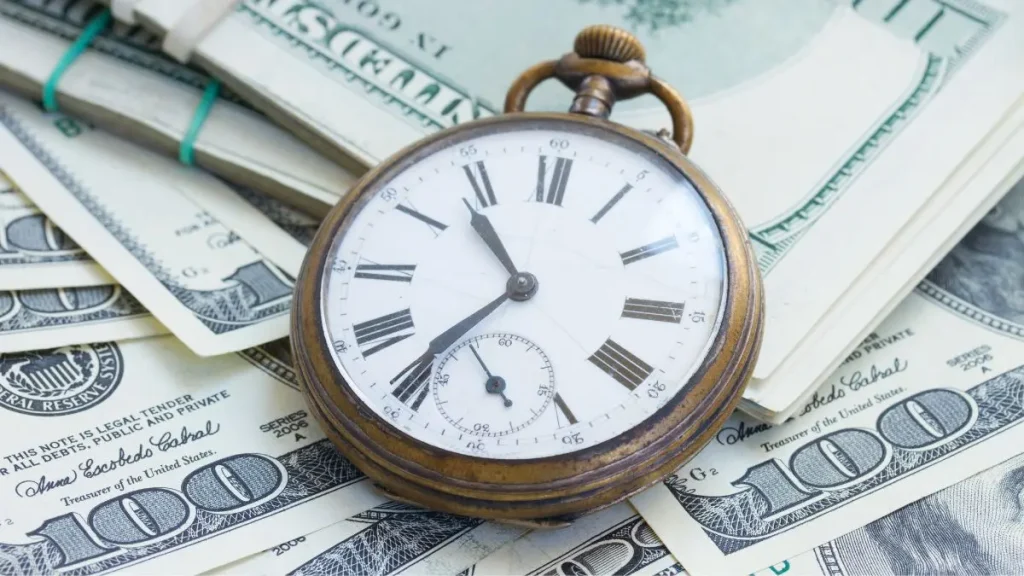 Old pocket watch lying on top of dollar bills representing time and money