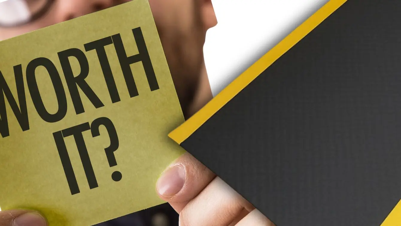 Close up of a hand holding a note that says worth it next to the edge of an anti fatigue mat. Hero Picture for an article that answers the question Are Anti Fatigue Mats Worth It