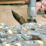 Stacks of cash on a workbench with a power tool, illustrating how much does it cost to start woodworking and why beginners often overestimate it