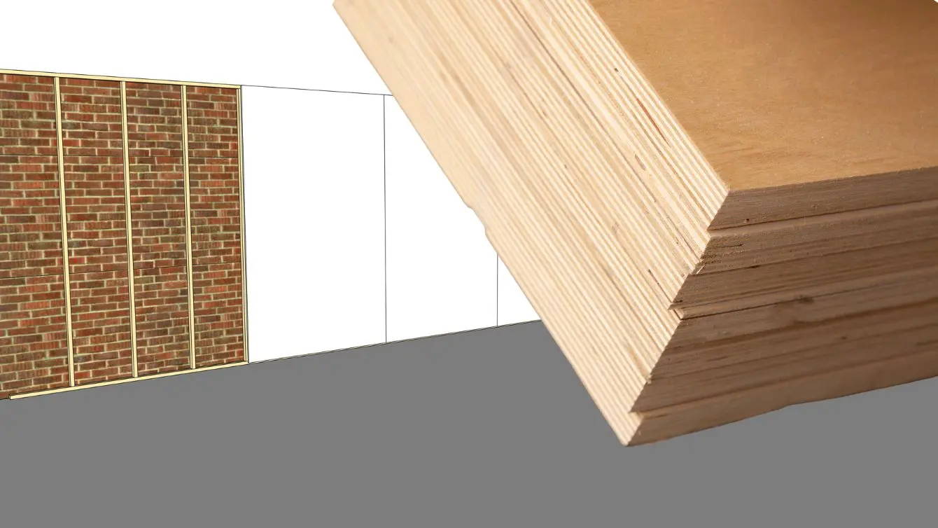 Plywood shop walls being installed in a small workshop, showing stacked plywood sheets and a framed wall.