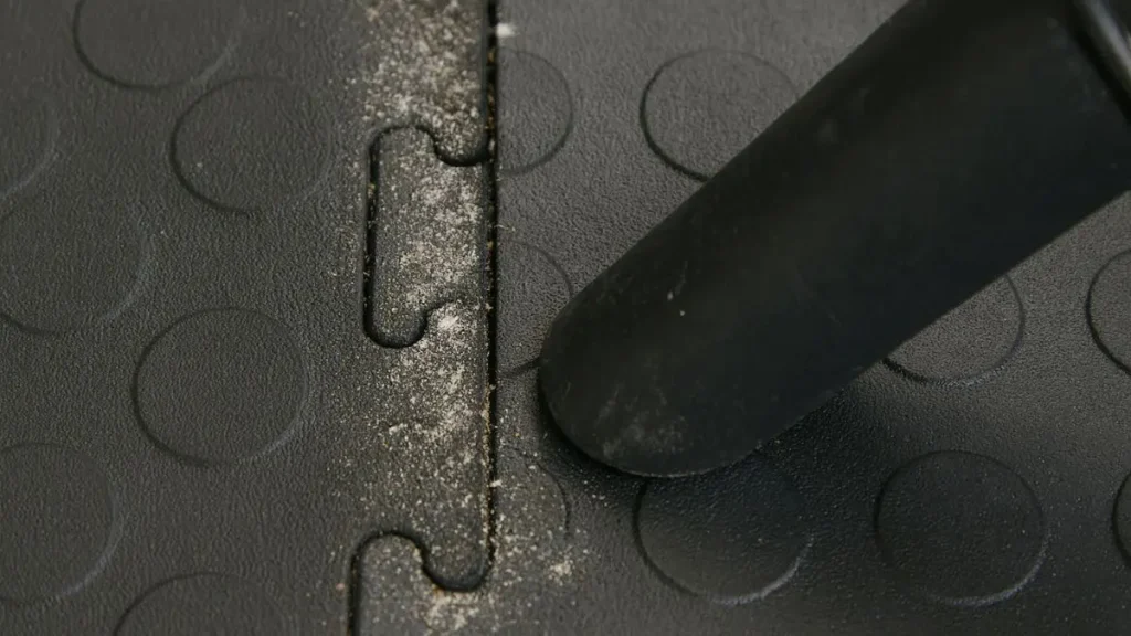 Close-up showing fine dust buildup between seams, illustrating the pros and cons of interlocking floor tiles in a woodworking shop.