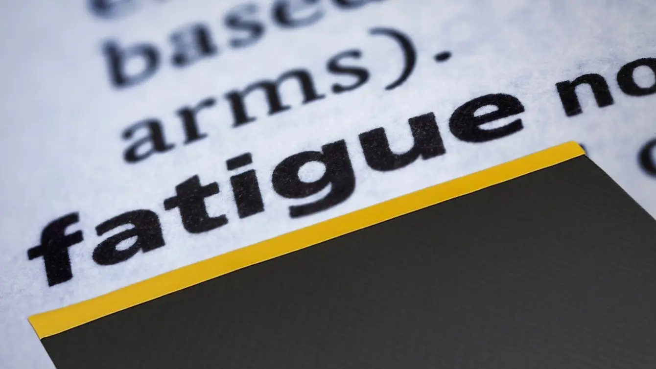 Close up of the word fatigue above the yellow edge of an anti fatigue mat, highlighting what an anti fatigue mat looks like in a woodshop so people understand what is an anti fatigue mat.